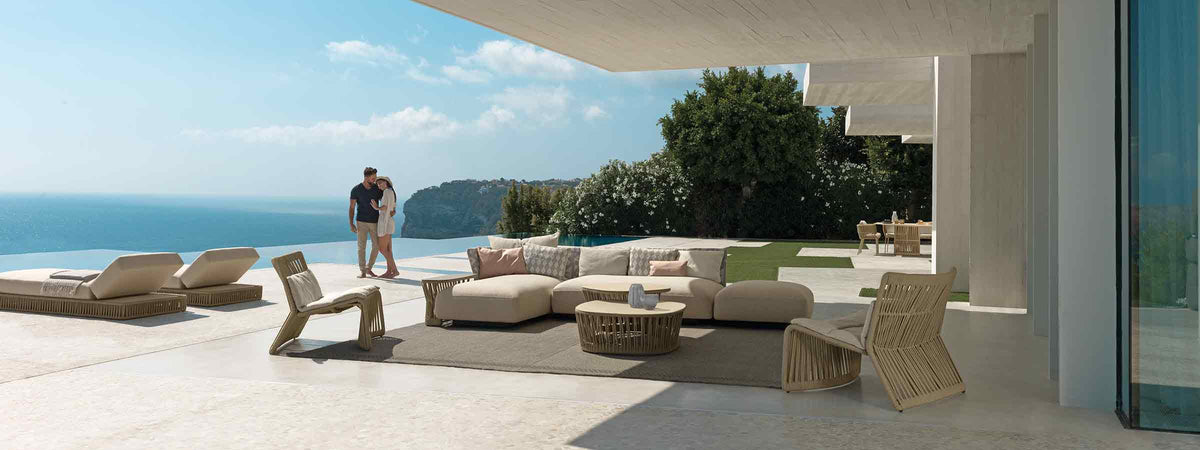A luxurious, sun-drenched Italian patio overlooking the Mediterranean sea, styled with high-end contemporary outdoor lounge furniture and artisanal decor.