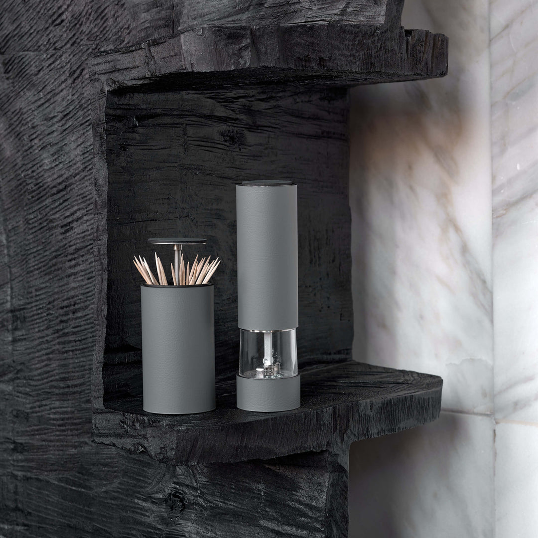 Two cylindrical containers on a dark stone shelf with a marble wall background