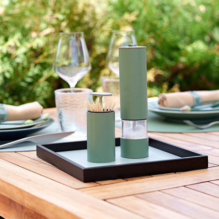 Green salt and pepper shakers on a tray with cutlery holder on a wooden table outdoors.