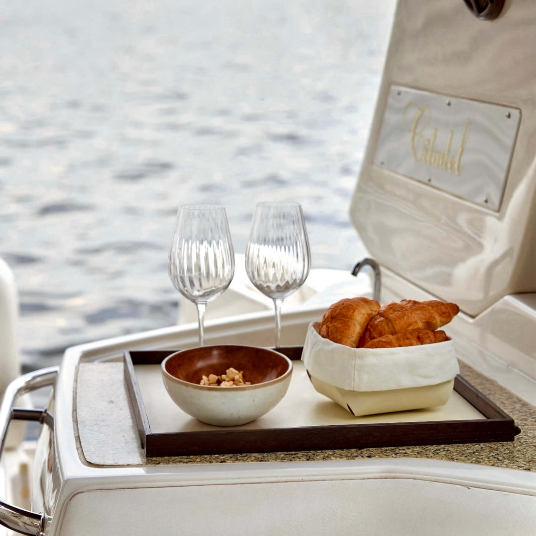 Tray with croissants and wine glasses on a boat with water in the background