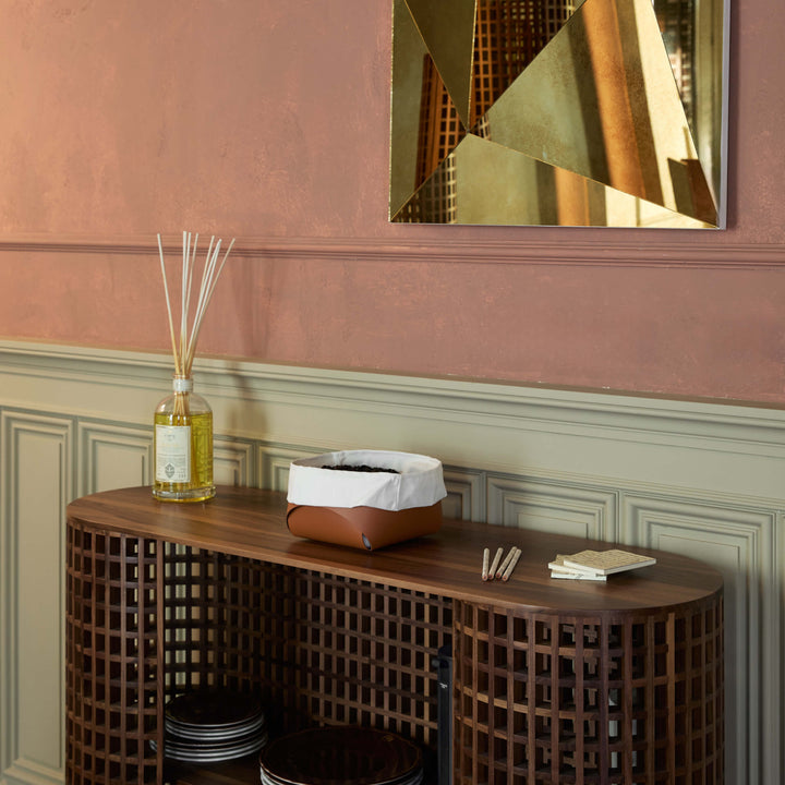 Wooden console table with decorative items against a pink wall with geometric mirror