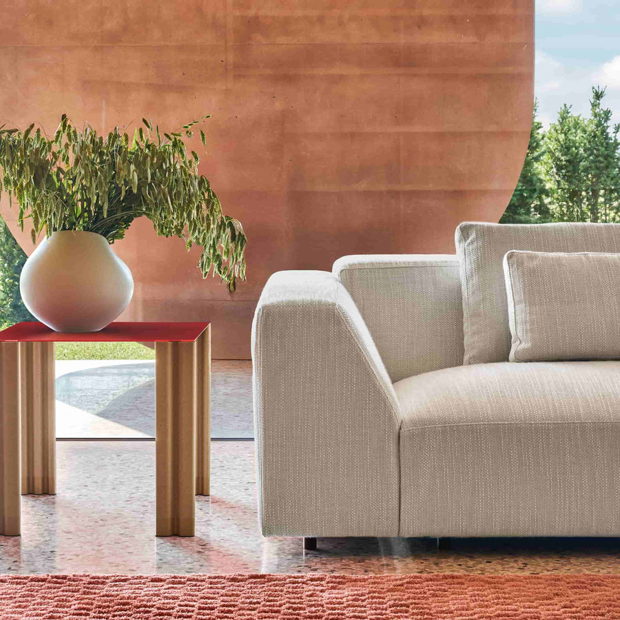 Beige sofa with a red side table and plant in a modern outdoor setting.